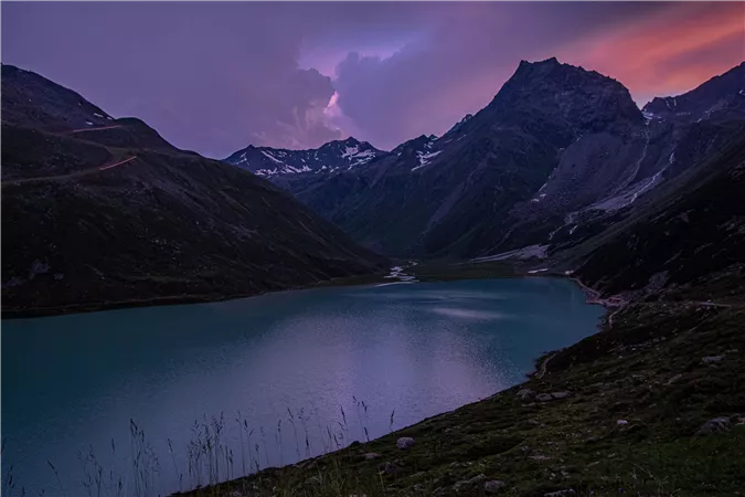 A tranquil mountain lake surrounded by majestic mountains under a colorful evening sky. The landscape radiates a peaceful atmosphere.