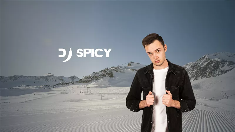 A young man stands in a winter landscape with snow-covered mountains in the background. The image displays the name "DJ SPICY" in modern lettering.