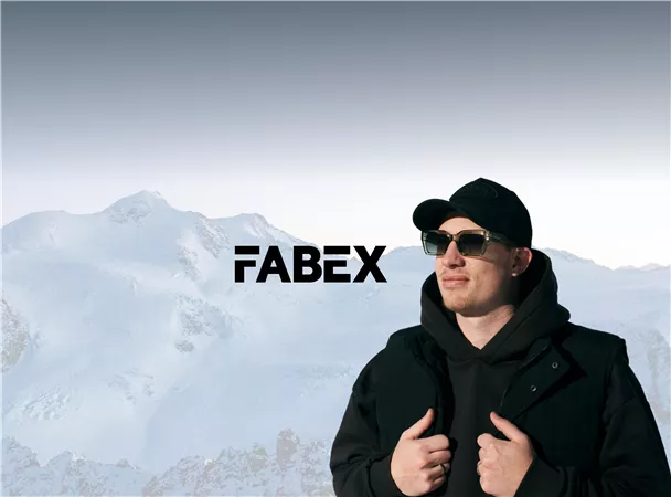 Ein Mann steht vor einer schneebedeckten Berglandschaft und trägt Sonnenbrillen. Im Hintergrund ist der Schriftzug "FABEX" zu sehen.