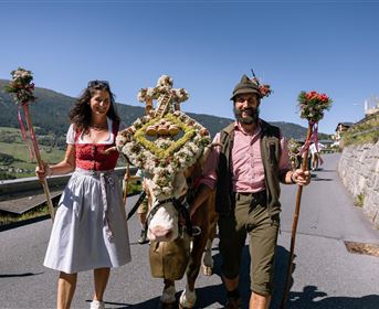 Ein traditionelles Fest mit einem festlich geschmückten Pferd und zwei Menschen in Trachten. Die Umgebung ist ländlich und die Atmosphäre ist festlich und fröhlich.