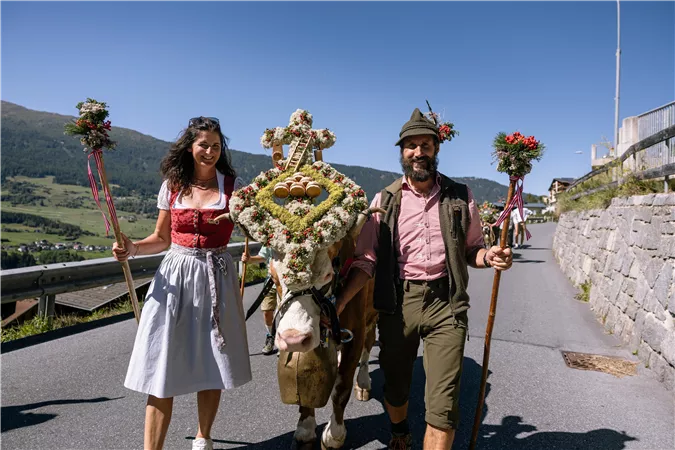 Ein traditionelles Fest mit einem festlich geschmückten Pferd und zwei Menschen in Trachten. Die Umgebung ist ländlich und die Atmosphäre ist festlich und fröhlich.