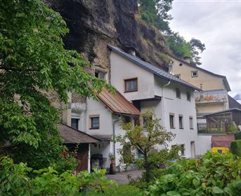 A typical house in a natural environment with rocks in the background. The area is green and surrounded by trees.