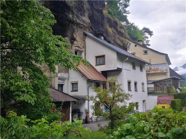 A typical house in a natural environment with rocks in the background. The area is green and surrounded by trees.