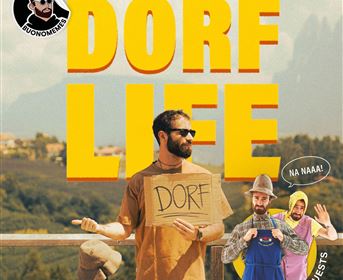 Ein humorvolles Plakat für eine Comedy-Show namens "Dorf Life". Es zeigt einen Mann mit einem Schild und zwei weitere Personen in bunten Kostümen im Hintergrund.