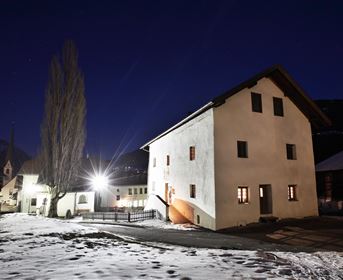 A quiet village at night with a snow-covered ground. The buildings are lit up and the sky is clear.