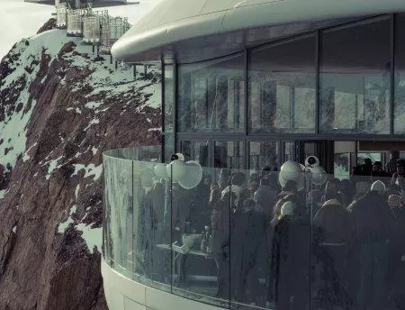 A modern glass facade with many people gathering in a snow-covered mountain area. In the background, rocks and snow can be seen.