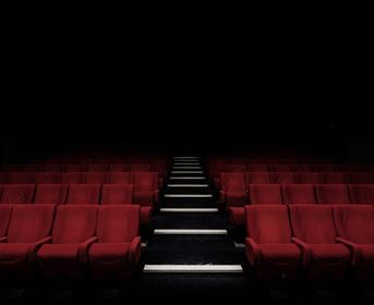 Ein dunkles Kino mit roten Sitzen. Der Weg in der Mitte ist gut beleuchtet.
