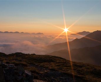 Ein atemberaubender Sonnenaufgang über den Bergen. Die Sonne strahlt über den Wolken und vermittelt ein Gefühl von Ruhe und Weite.