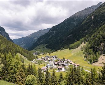 Eine malerische Berglandschaft mit einem kleinen Dorf in einem Tal. Umgeben von hohen Bergen und grünen Wäldern.