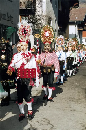 Eine traditionelle Parade mit kostümierten Teilnehmern. Sie tragen farbenfrohe Masken und Blumenkränze.