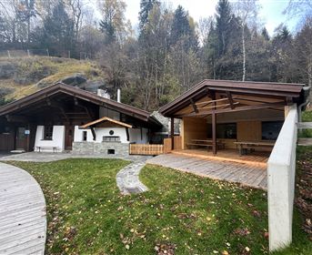 Two modern wooden buildings in a natural environment. The front area is designed with green spaces and wooden terraces.