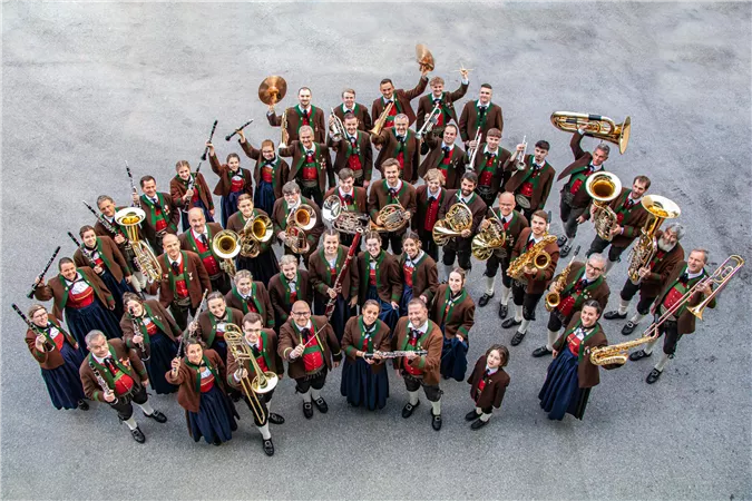Eine Gruppe von Musikern steht zusammen und präsentiert ihre Instrumente. Sie tragen traditionelle Trachten und lächeln in die Kamera.