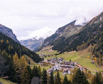 Eine malerische Berglandschaft mit einem kleinen Dorf im Tal. Umgeben von hohen Bergen und bunten Wäldern.