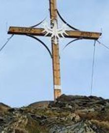 A large wooden cross stands on a rocky hill. The sky is clear and blue, creating a calm atmosphere.