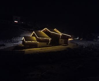 A snowy house adorned with warm lights at night. The surroundings are dark and quiet.