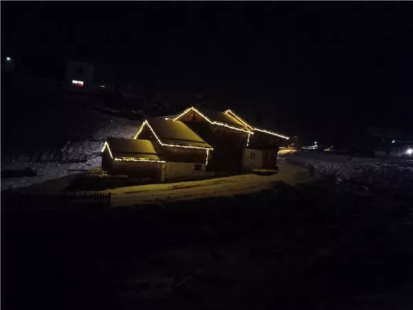 Ein gemütliches Haus im Schnee, das mit Lichtern geschmückt ist. Die Szene ist nachts und vermittelt eine festliche Atmosphäre.