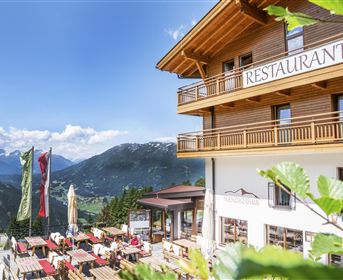 Ein gemütliches Restaurant in den Bergen mit Terrassenplätzen und Blick auf die Natur. Klare blaue Himmel und grüne Umgebung schaffen eine einladende Atmosphäre.
