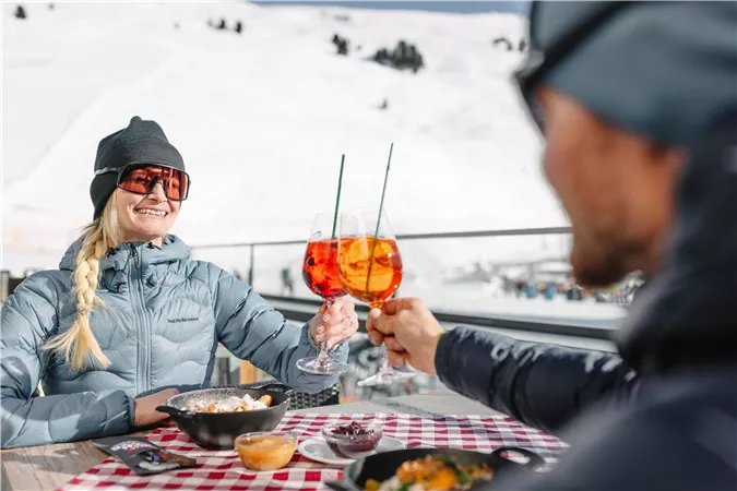 Ein Paar stoßt mit einem Glas Aperol auf den Skitag an.