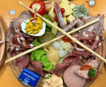 Eine appetitliche Platte mit verschiedenen Wurst- und Käsesorten, frischem Gemüse und dekorativen Beilagen. Die Speisen sind ansprechend angeordnet und mit Stäbchen dekoriert.