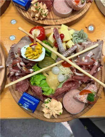 A delicious platter with various types of sausages and cheeses, fresh vegetables, and decorative side dishes. The foods are attractively arranged and adorned with sticks.