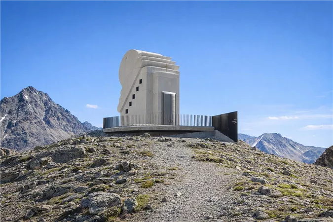 Ein modernes Gebäude steht auf einem Berg, umgeben von felsiger Landschaft. Der klare Himmel und die majestätischen Berge im Hintergrund verleihen der Szene eine beeindruckende Atmosphäre.