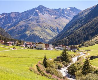 A picturesque mountain landscape with green meadows and a clear river. In the background, the majestic mountains rise.