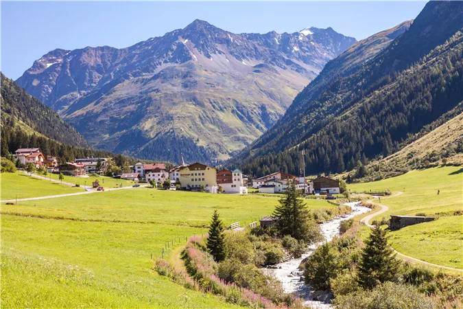 A picturesque mountain landscape with green meadows and a clear river. In the background, the majestic mountains rise.