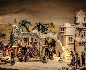 A detailed nativity scene with figures depicting the birth of Jesus. In the background, buildings and trees can be seen in a rural landscape.
