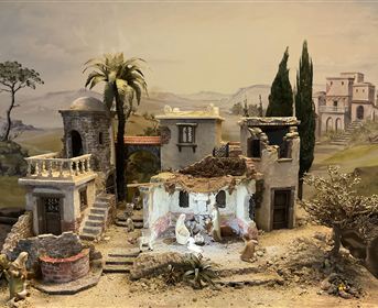 A detailed miniature of a village-like scenario with ruined buildings and palm trees. In the foreground, figures can be seen reenacting a scene.