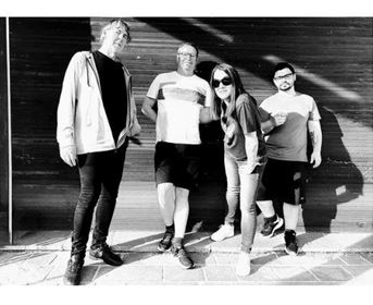 A group of four people is standing in front of a wall. They are smiling and posing in a black-and-white picture.