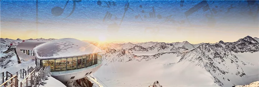 Ein modernes Gebäude mit Rundungen in der schneebedeckten Berglandschaft. Die Sonne geht hinter den Bergen auf und verbreitet eine warme Atmosphäre.