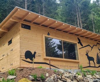 Eine moderne Holzhütte im Wald, geschmückt mit Tiermotiven. Umgeben von Bäumen und Natur, vermittelt sie ein rustikales, einladendes Gefühl.
