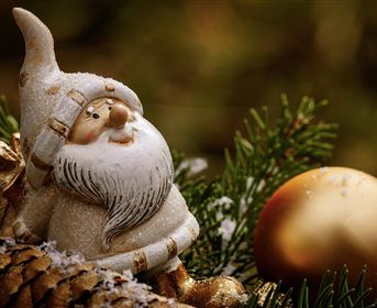 Eine festliche Dekoration mit einem Weihnachtsmann aus Keramik und einer goldenen Kugel. Der Hintergrund zeigt grünes Tannenzweigholz.
