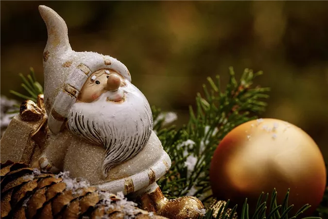 A festive decoration featuring a ceramic Santa Claus and a golden ball. The background displays green fir tree wood.