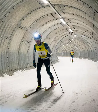 Ein Sportler fährt auf Skiern durch einen beleuchteten Tunnel. Im Hintergrund ist ein weiterer Skifahrer zu sehen.