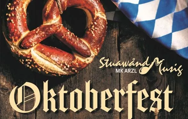 Eine große Brezel auf einem Holztisch, umgeben von traditioneller bayerischer Dekoration. Der Schriftzug "Oktoberfest" hebt die festliche Stimmung hervor.