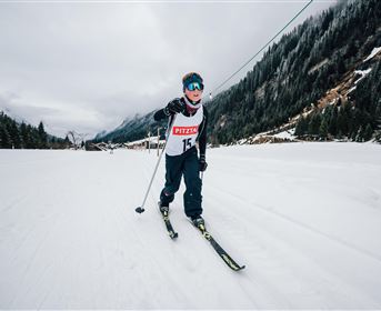 A skier is skiing on a snowy slope. In the background, snow-covered mountains and wooded hills can be seen.