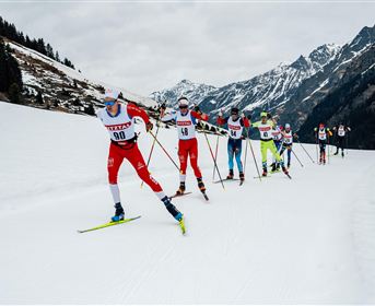 A group of skiers is riding on a snowy track in the mountains. In the background, impressive snow-covered mountains are visible.