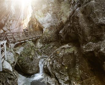 Ein charmantes Haus, das an einen Felsen gebaut ist, umgeben von grünen Bäumen. Der Himmel ist bewölkt und die Umgebung wirkt ruhig und ländlich.