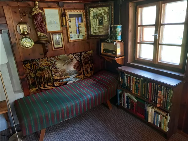 Ein gemütlicher Raum mit einer Bank, Regalen voller Bücher und vintage Deko an der Wand. Das Fenster lässt viel Tageslicht herein und schafft eine einladende Atmosphäre.