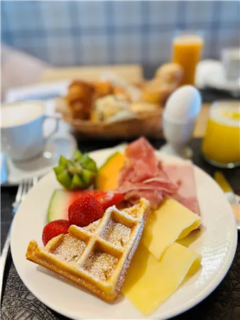 Ein reichhaltiges Frühstücksarrangement mit Waffeln, frischen Früchten, Brot und Aufschnitt. Dazu gibt es Kaffee und Orangensaft.