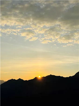 Sonnenaufgang über den Bergen mit goldenen Strahlen am Horizont. Der Himmel ist mit sanften Wolken bedeckt.
