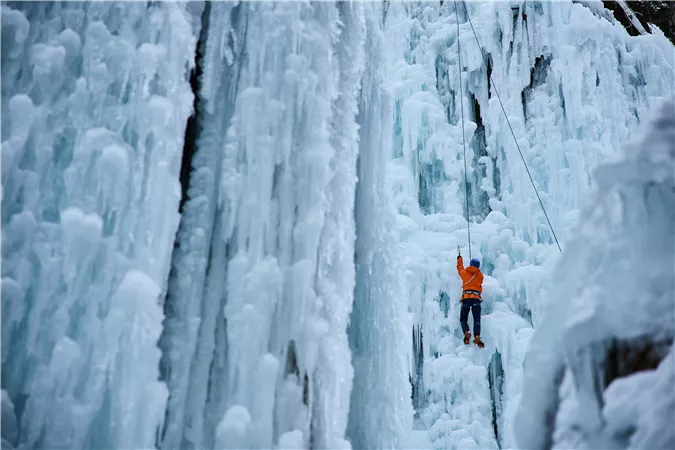 Ein Eiskletterer steigt an einer gefrorenen Wasserwand auf. Die Umgebung ist von frostigen Eisformationen umgeben.