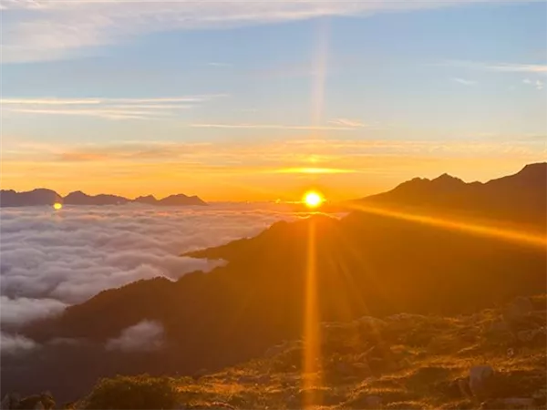 Ein atemberaubender Sonnenaufgang über den Bergen. Die Wolken liegen sanft unterhalb des Gebirges und erhellen die Landschaft.