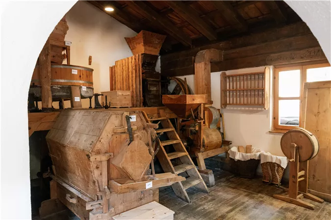 A traditional mill interior with wooden furniture and various utensils. The atmosphere is rustic and reflects the historical use.