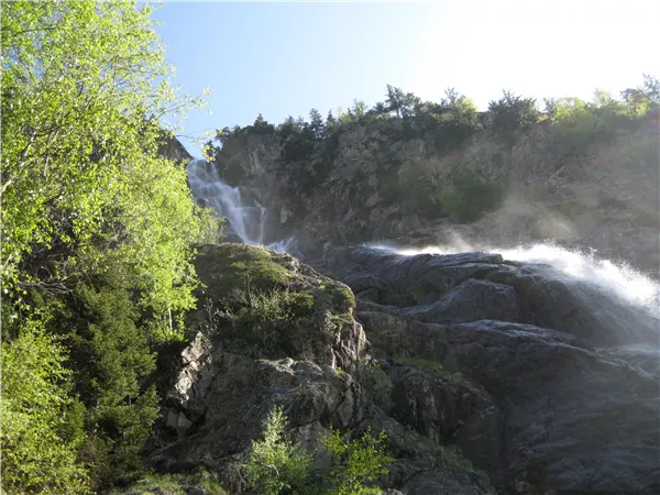 A beautiful waterfall cascades over rocky cliffs. Surrounded by green trees and radiant sunlight.