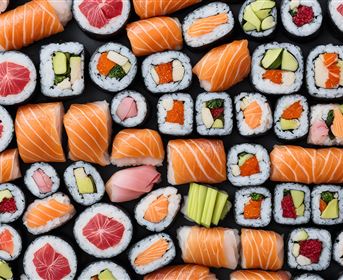A colorful selection of sushi rolls is laid out on a black background. The variety ranges from tuna and salmon to vegetables and other fillings.