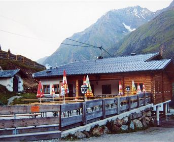 A cozy wooden mountain cabin in a picturesque mountain landscape.
Surrounded by mountains and with outdoor seating, it is an inviting place for guests.