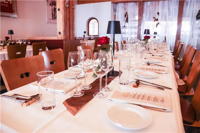 An elegantly set dining table in a restaurant with glasses, plates, and cutlery. Decorative roses and candles create a festive atmosphere.