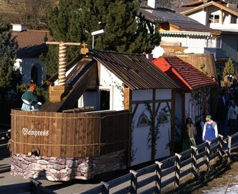 A traditional wooden building with a red roof and a small wooden structure in front. People are standing nearby and enjoying the surroundings.